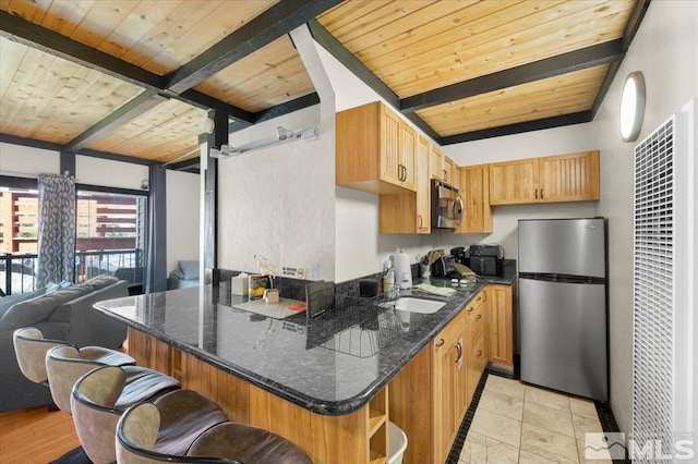 kitchen featuring wooden ceiling, stainless steel appliances, open floor plan, dark stone counters, and a kitchen bar