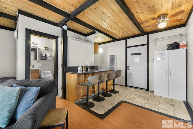 kitchen featuring dark countertops, wooden ceiling, ceiling fan, a kitchen breakfast bar, and beam ceiling