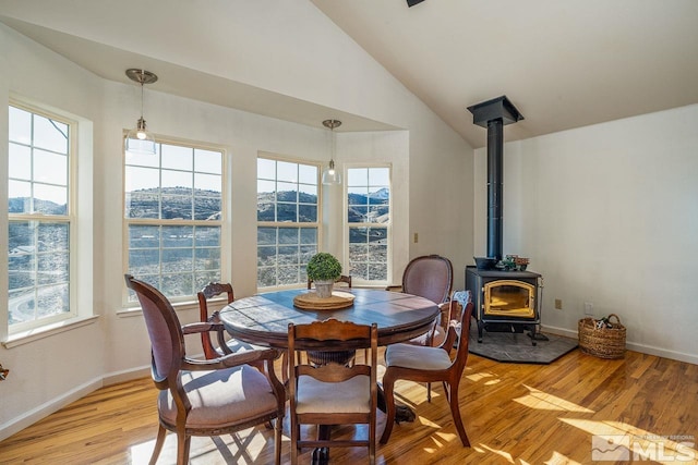 dining area with vaulted ceiling, a wood stove, plenty of natural light, and light wood-style flooring