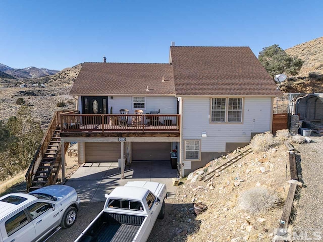 view of front of property featuring a deck with mountain view, an attached garage, stairs, driveway, and a patio area