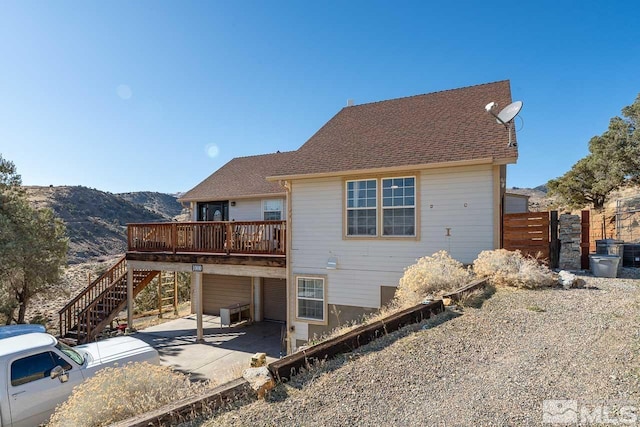 back of house with a deck with mountain view, fence, stairway, a carport, and a patio area