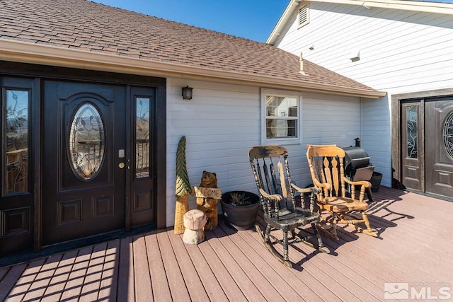 doorway to property with a deck and roof with shingles