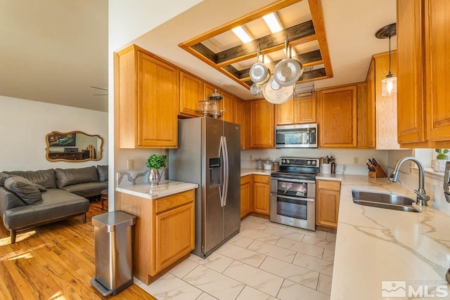 kitchen featuring appliances with stainless steel finishes, brown cabinetry, open floor plan, a sink, and coffered ceiling