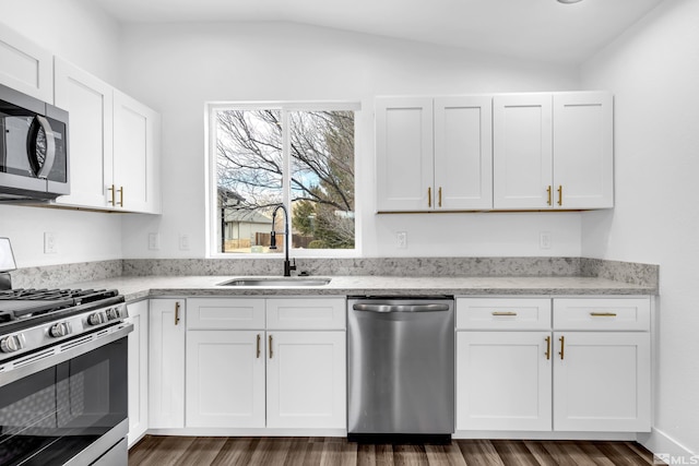 kitchen with light stone counters, a sink, white cabinets, vaulted ceiling, and appliances with stainless steel finishes