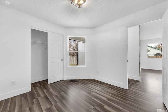 unfurnished bedroom featuring a textured ceiling, visible vents, baseboards, a closet, and dark wood finished floors