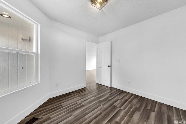 empty room featuring dark wood-style flooring, a textured ceiling, and baseboards