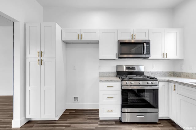 kitchen featuring light stone counters, dark wood-style floors, appliances with stainless steel finishes, white cabinets, and baseboards