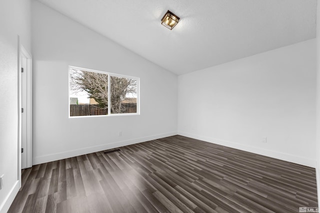 spare room with dark wood-type flooring, lofted ceiling, and baseboards