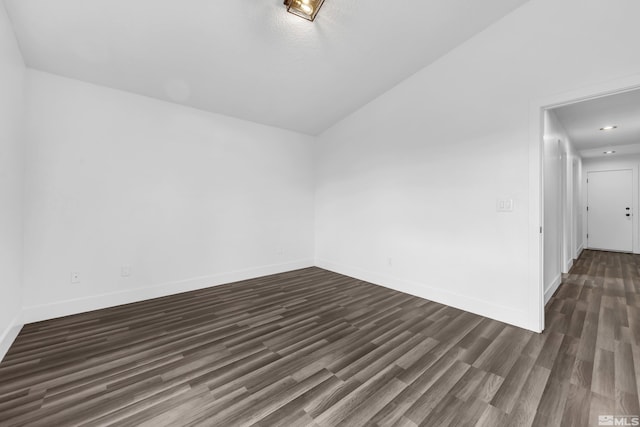 spare room with dark wood-type flooring, lofted ceiling, and baseboards