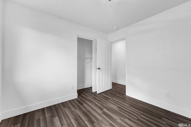 unfurnished bedroom with dark wood-style floors, a textured ceiling, baseboards, and a closet