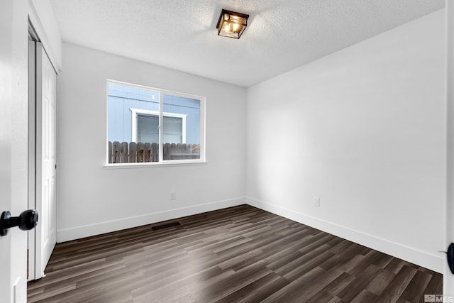 unfurnished bedroom with a textured ceiling, visible vents, baseboards, a closet, and dark wood finished floors