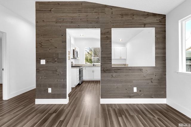 interior space featuring wooden walls, baseboards, vaulted ceiling, and dark wood-type flooring