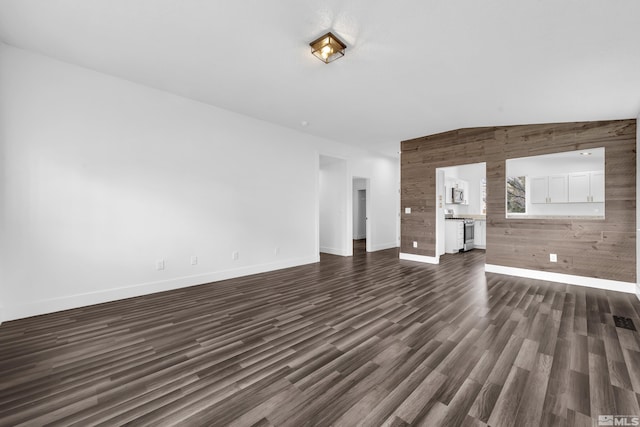 unfurnished living room with lofted ceiling, baseboards, dark wood finished floors, and wooden walls