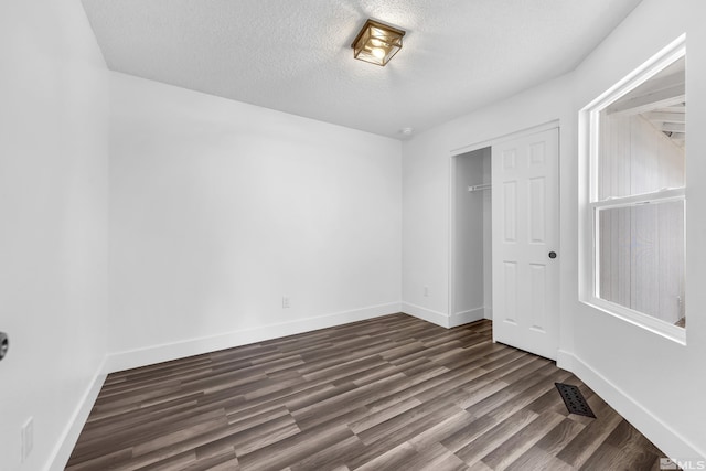 unfurnished bedroom with a textured ceiling, dark wood-style flooring, a closet, and baseboards