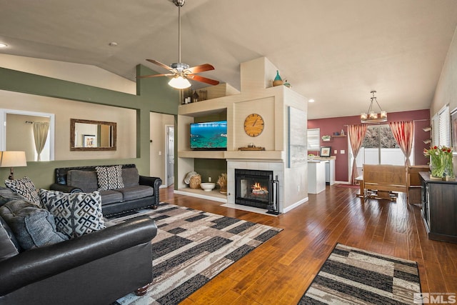 living room featuring baseboards, lofted ceiling, wood-type flooring, a fireplace, and ceiling fan with notable chandelier