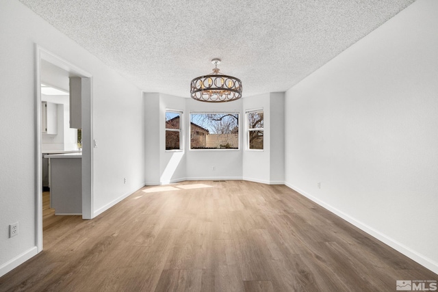 unfurnished dining area with an inviting chandelier, a textured ceiling, baseboards, and wood finished floors