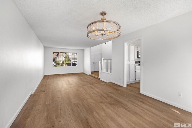 unfurnished living room with a notable chandelier, a textured ceiling, baseboards, and wood finished floors