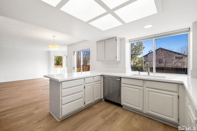 kitchen featuring a peninsula, stainless steel dishwasher, light wood-type flooring, and a sink