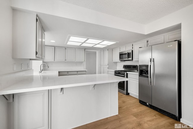 kitchen featuring a peninsula, stainless steel appliances, a textured ceiling, light countertops, and light wood-type flooring