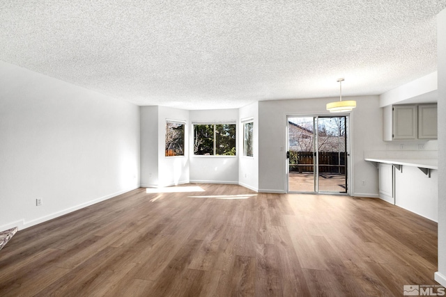 unfurnished living room featuring a textured ceiling, baseboards, and wood finished floors