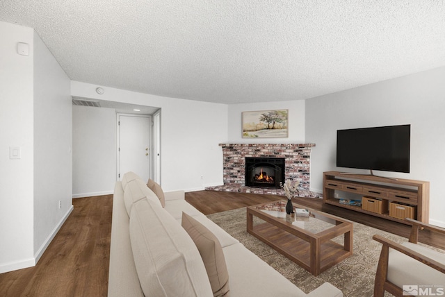 living area with a textured ceiling, wood finished floors, visible vents, baseboards, and a brick fireplace