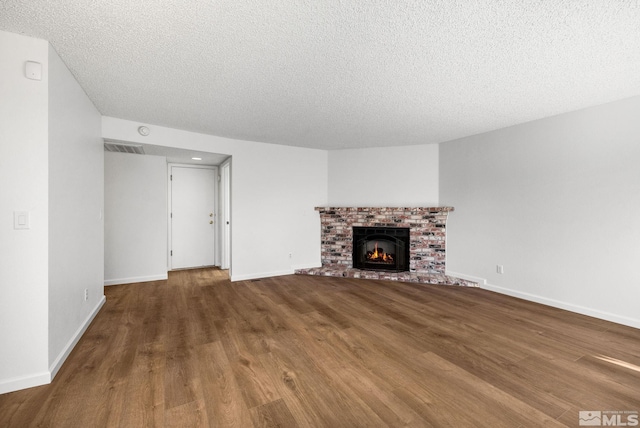 unfurnished living room with visible vents, a brick fireplace, a textured ceiling, wood finished floors, and baseboards