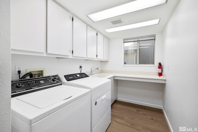 clothes washing area with cabinet space, visible vents, a sink, wood finished floors, and washer and dryer