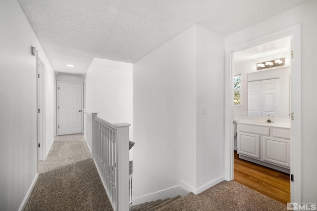 hall featuring a textured ceiling, carpet floors, an upstairs landing, and baseboards