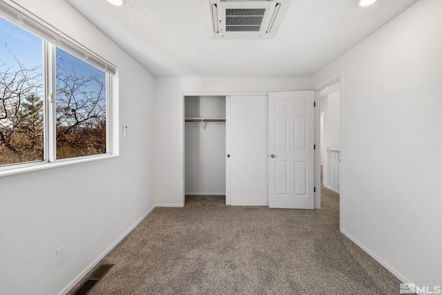 unfurnished bedroom featuring a textured ceiling, carpet floors, visible vents, and baseboards