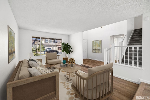 living area with a textured ceiling, stairway, wood finished floors, and baseboards