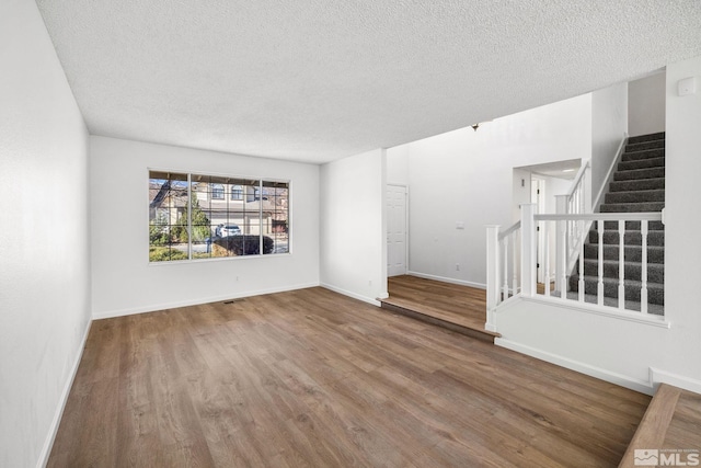 unfurnished living room featuring a textured ceiling, stairway, wood finished floors, and baseboards