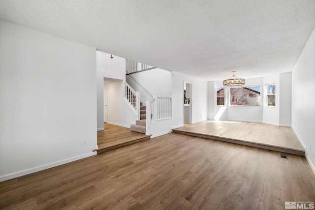 unfurnished living room featuring a textured ceiling, stairway, baseboards, and wood finished floors