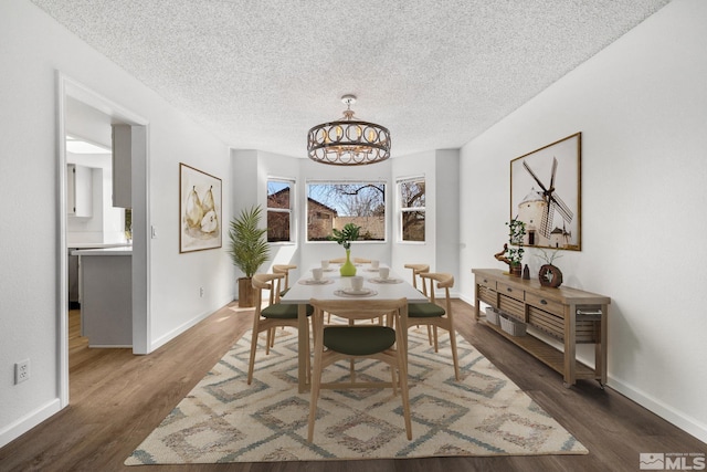 dining area with dark wood-style floors, a notable chandelier, baseboards, and a textured ceiling