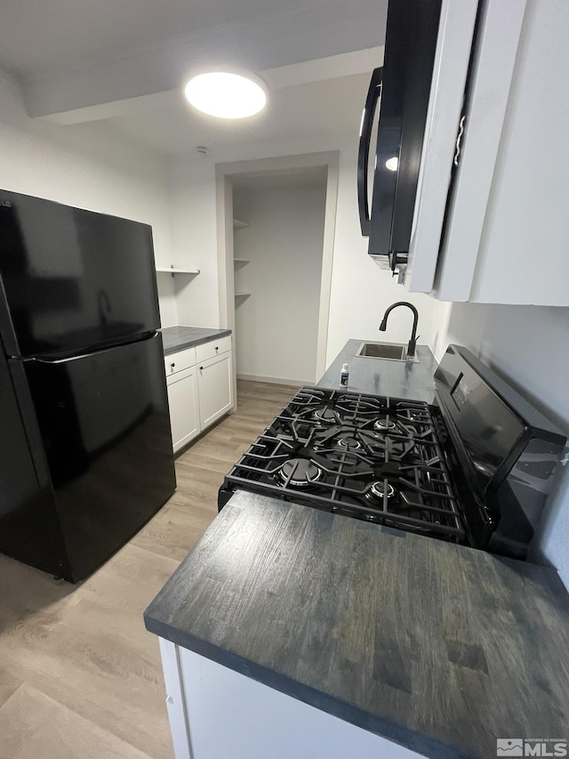 kitchen featuring light wood finished floors, dark countertops, black appliances, white cabinetry, and a sink