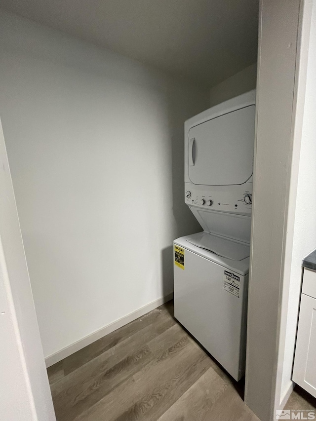 laundry area featuring laundry area, light wood-style flooring, stacked washer and clothes dryer, and baseboards