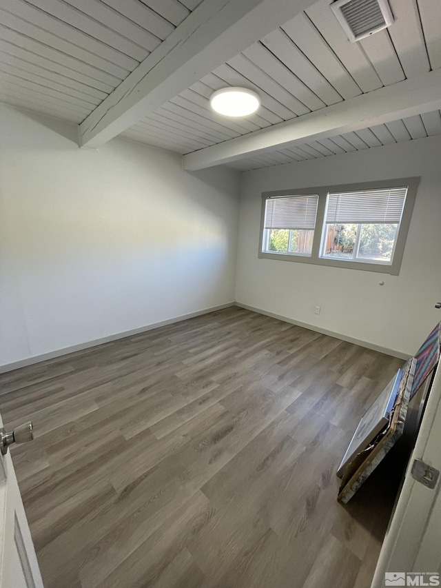 empty room featuring visible vents, beamed ceiling, baseboards, and wood finished floors