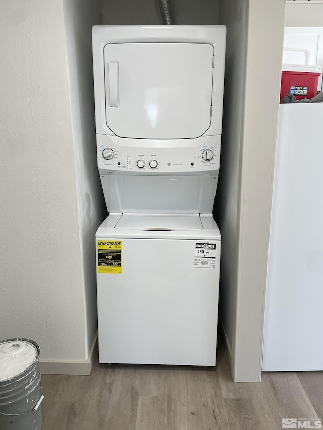 laundry area featuring laundry area, wood finished floors, stacked washer and clothes dryer, and baseboards