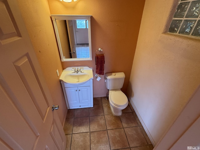 half bath featuring toilet, tile patterned floors, vanity, and baseboards