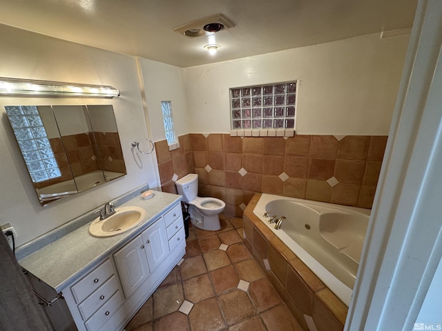 bathroom with tile walls, toilet, vanity, tile patterned flooring, and a tub with jets