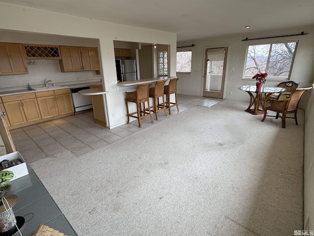 kitchen featuring light colored carpet, a sink, light countertops, appliances with stainless steel finishes, and a kitchen bar