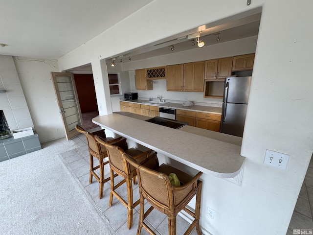 kitchen featuring light countertops, freestanding refrigerator, a sink, a peninsula, and a kitchen bar