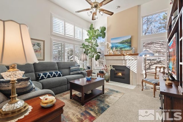 carpeted living area featuring a tiled fireplace, a high ceiling, and ceiling fan