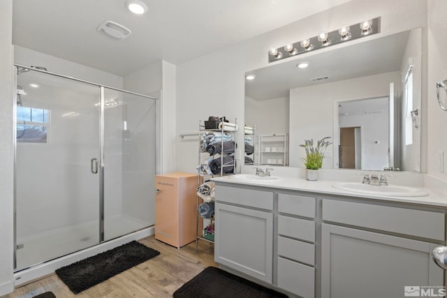 full bath featuring double vanity, a shower stall, a sink, and wood finished floors