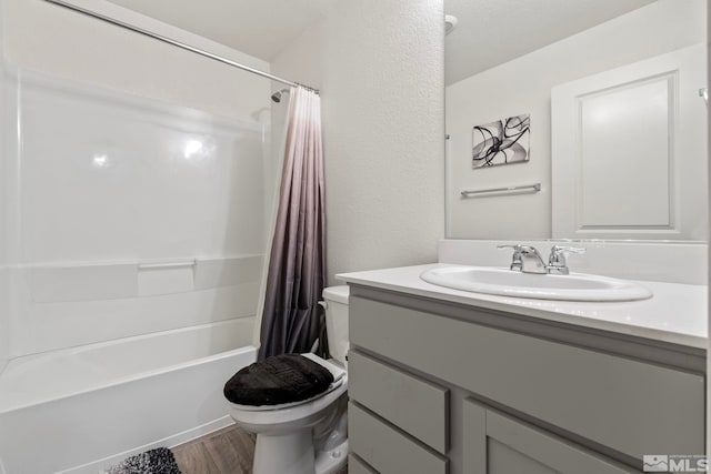 bathroom with a textured wall, toilet, wood finished floors, vanity, and shower / bath combo with shower curtain