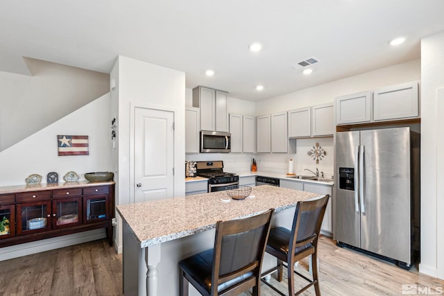 kitchen featuring stainless steel appliances, a kitchen island, a sink, gray cabinets, and light wood finished floors