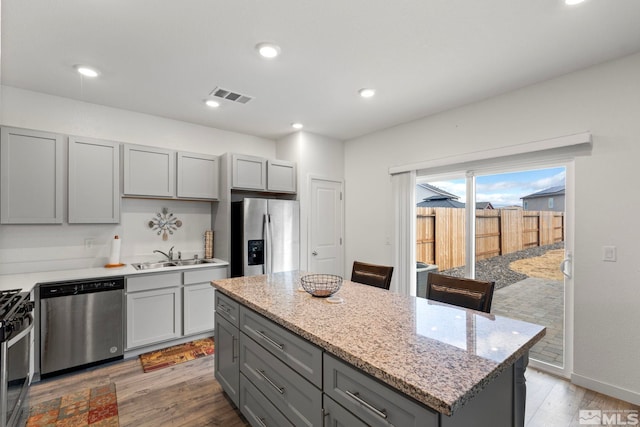 kitchen featuring visible vents, wood finished floors, stainless steel appliances, gray cabinetry, and a sink