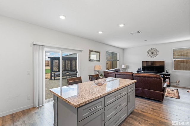 kitchen with visible vents, light stone counters, wood finished floors, a center island, and gray cabinetry