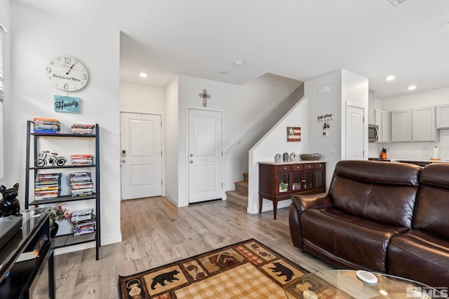 living room featuring light wood-type flooring, baseboards, recessed lighting, and stairs