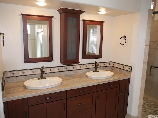 full bath featuring backsplash, a sink, a tile shower, and double vanity