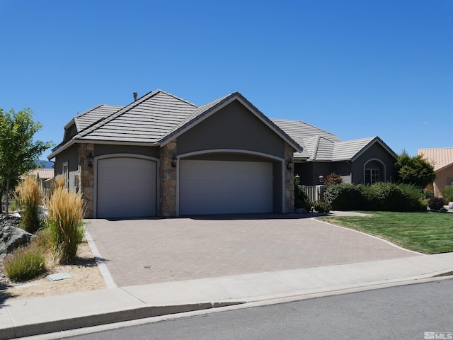 single story home with stone siding, a tiled roof, an attached garage, decorative driveway, and a front yard